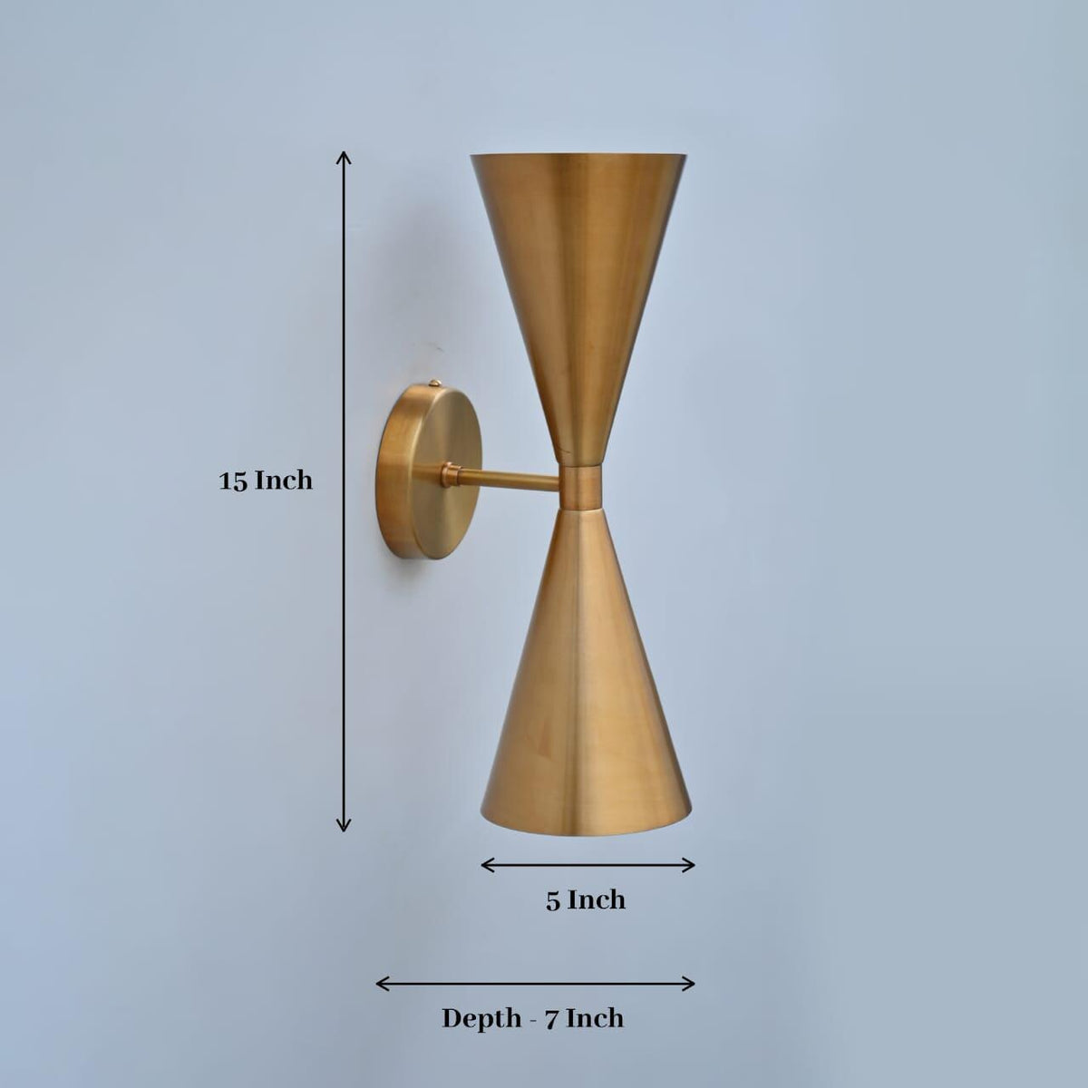 A wall-mounted sconce with a brushed brass finish, shown with dimension arrows and labels indicating a height of 15 inches, width of 5 inches, and depth of 7 inches against a light blue-gray background.