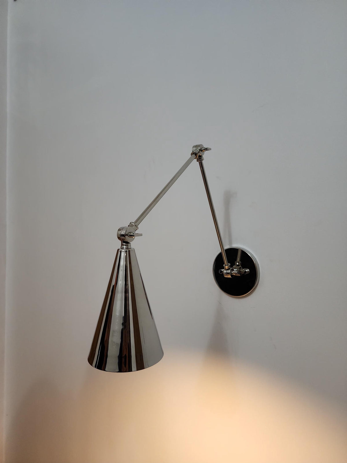 Adjustable brass wall lamp with cone design.