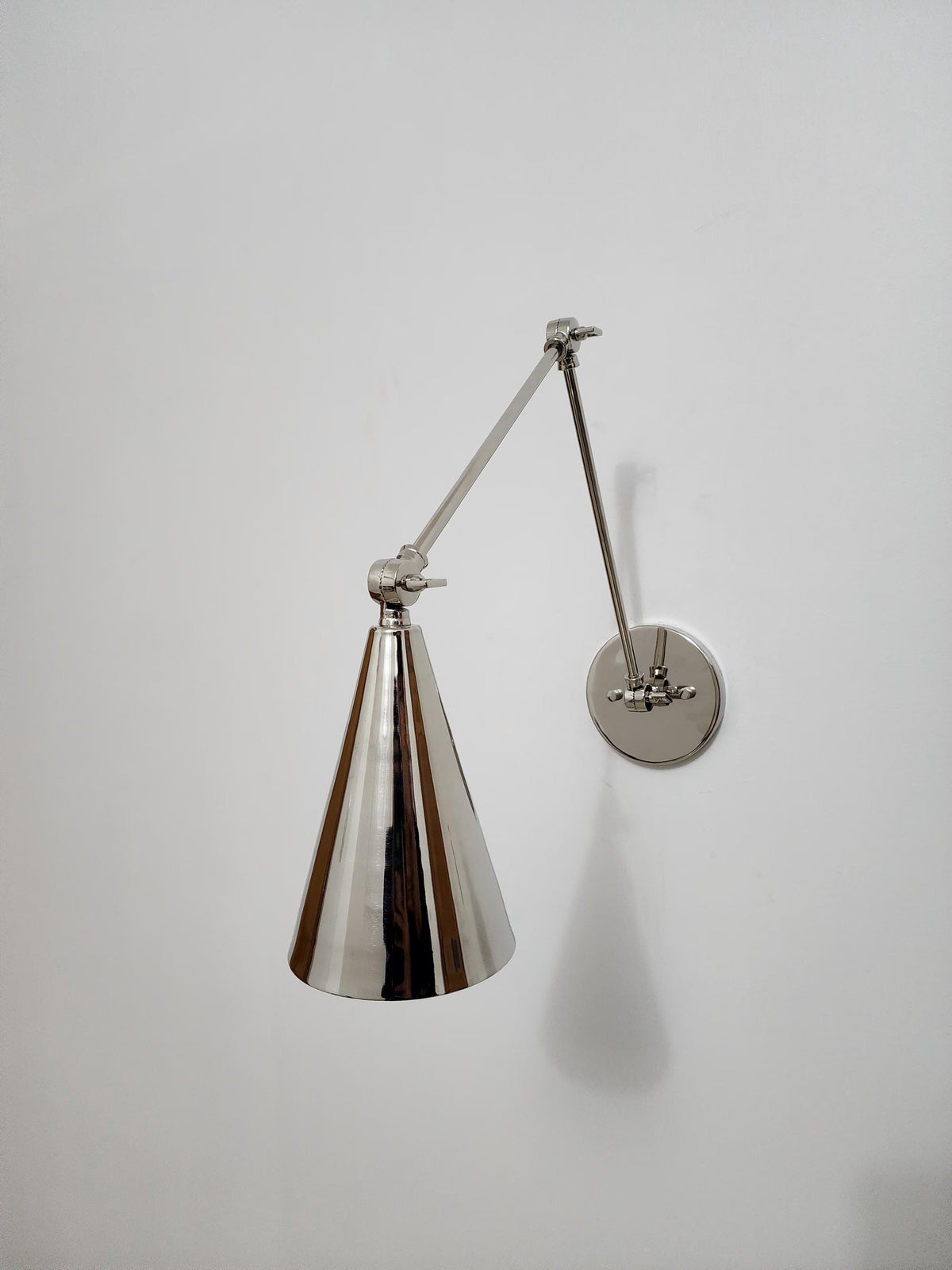 Adjustable brass wall sconce with cone shade.