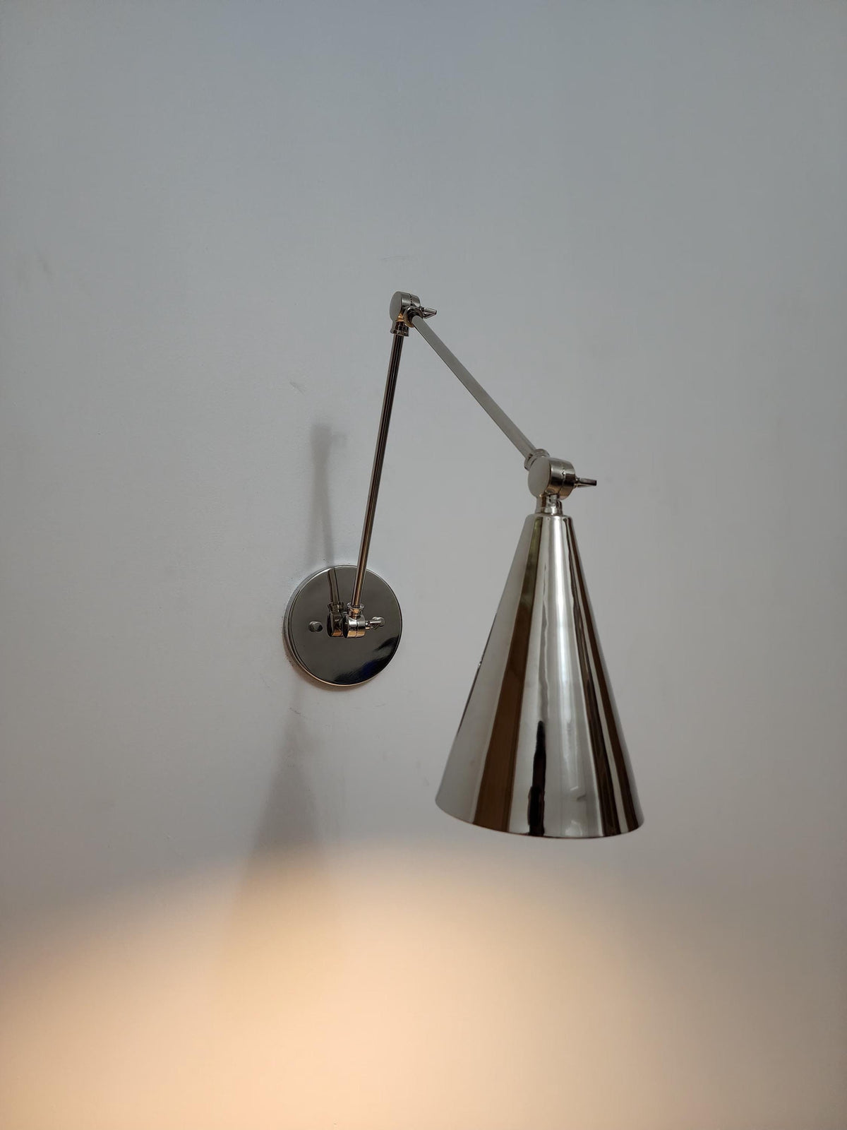 Articulated brass wall lamp with cone-shaped shade.