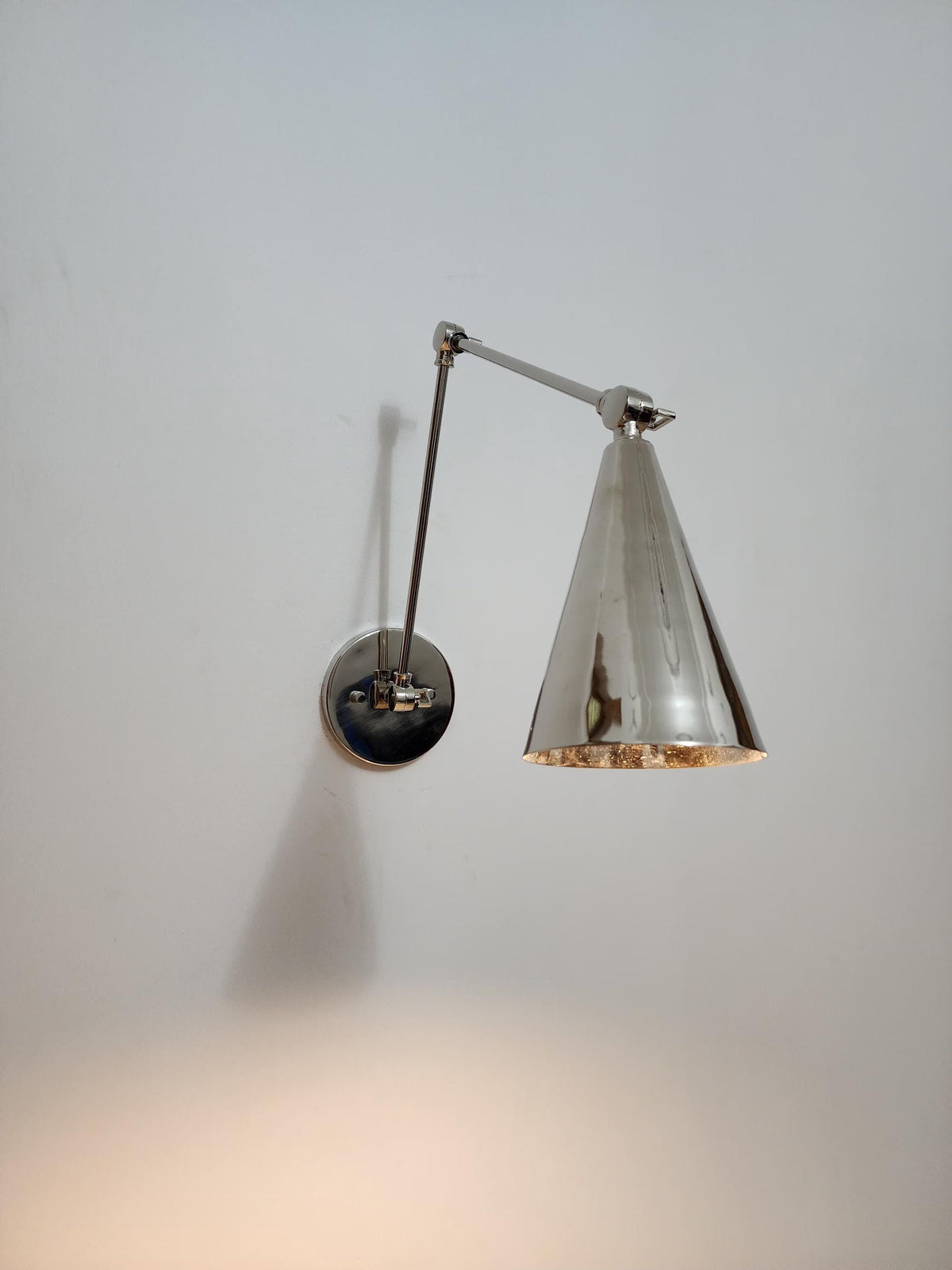 Brass cone wall sconce with adjustable arm.