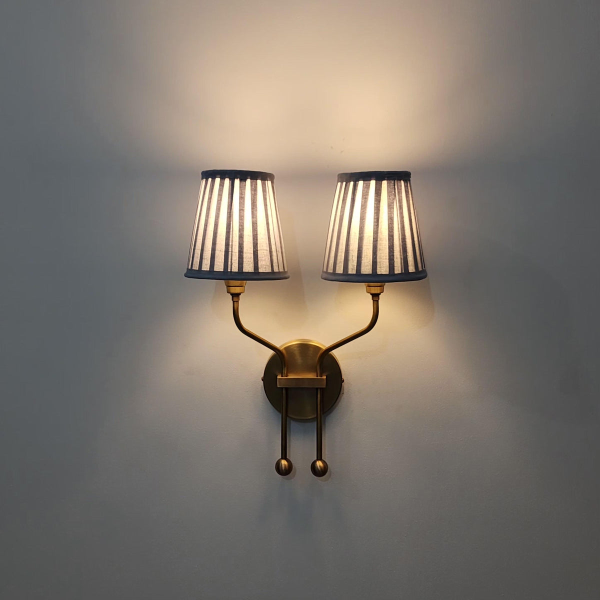 Brass double arm wall sconce with pleated shades.