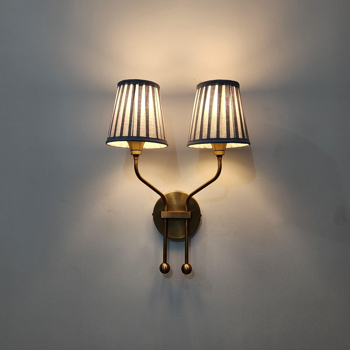 Double brass arm wall light with pleated shades.