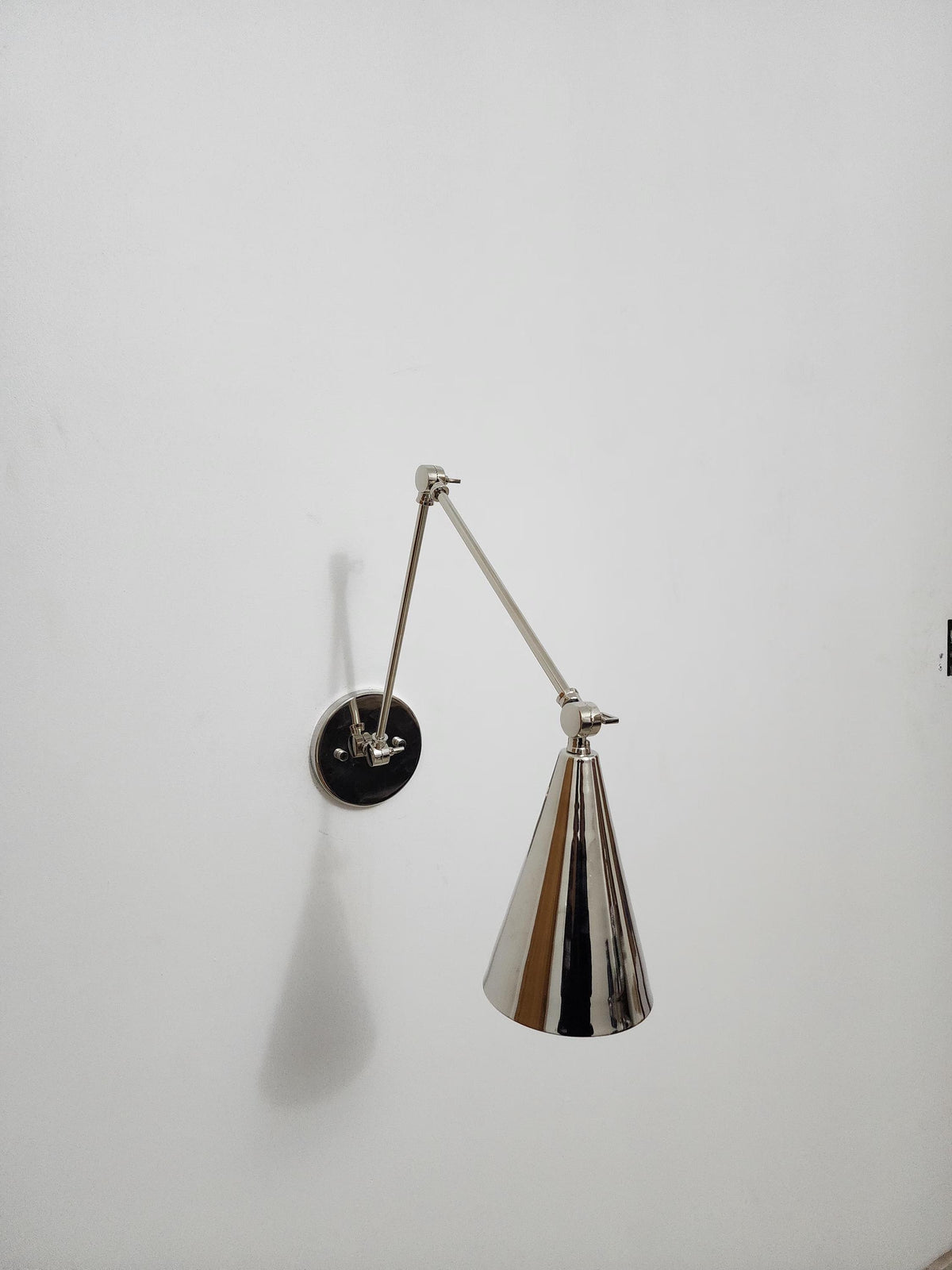Handmade adjustable brass wall lamp with cone shade.