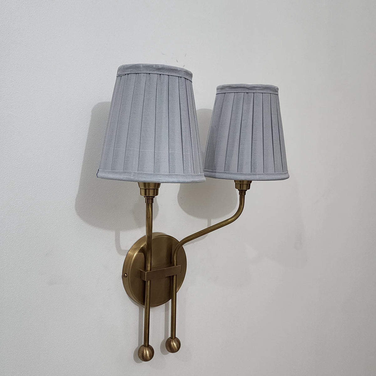 Brass wall sconce with two pleated shades and vintage design.