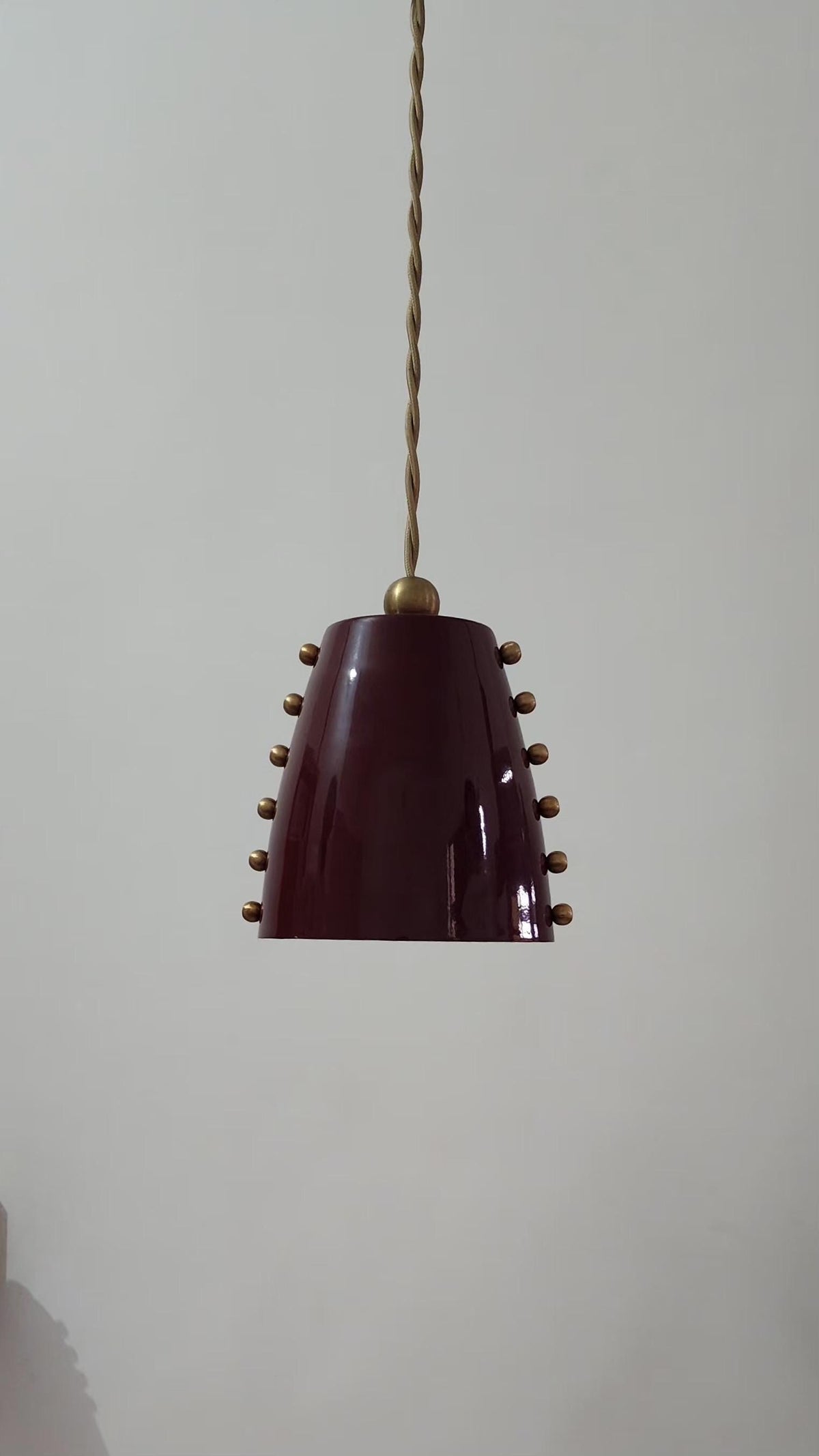 Vintage pendant light with a maroon shade and brass accents on a plain background